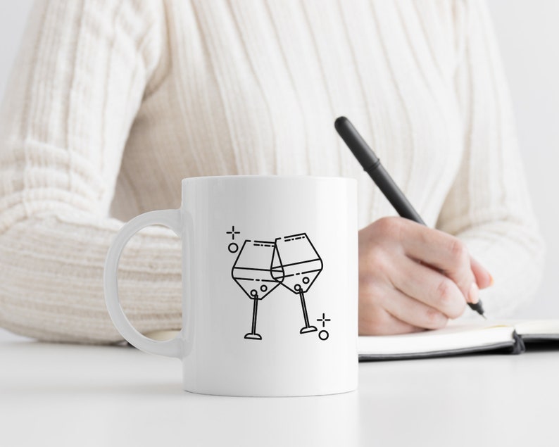 May include: White ceramic mug with a black line drawing of two wine glasses clinking together. The mug is on a white surface.