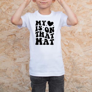 May include: White t-shirt with black text that reads "My &hearts; is on that mat".