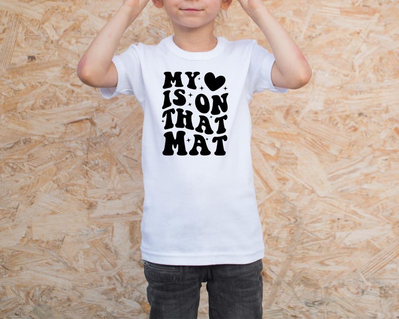 May include: White t-shirt with black text that reads "My &hearts; is on that mat".