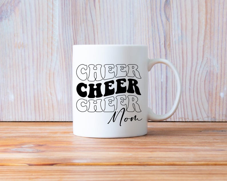 May include: White ceramic mug with black text that reads "Cheer Cheer Cheer Mom" in a retro font.