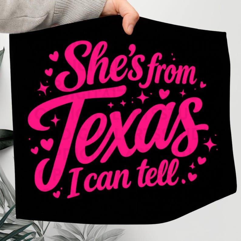 K&ouml;nnte beinhalten: Schwarzes Textil mit dem Text "She's from Texas I can tell" in leuchtendem Pink, umgeben von Herzen und Sternen. Das Design ist in einer verspielten, kursiven Schriftart gehalten.