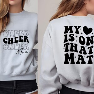 May include: Gray sweatshirt with black text that says "Cheer Cheer Cheer Mom" on the front and "My &hearts; is on that Mat" on the back.