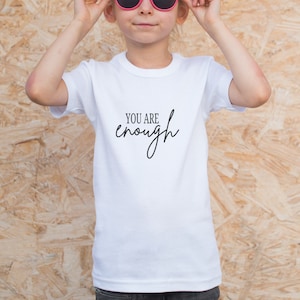 Pode incluir: Camiseta branca com o texto "You are enough" escrito em caligrafia preta.