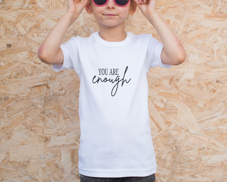 Pode incluir: Camiseta branca com o texto "You are enough" escrito em caligrafia preta.