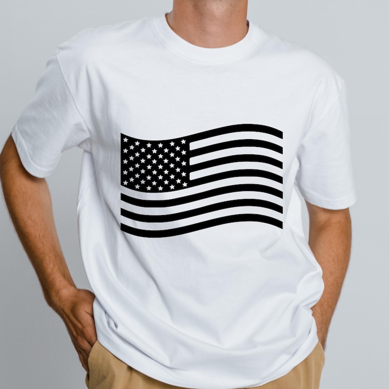 May include: White t-shirt featuring a black and white American flag design. The flag graphic includes stars and stripes, creating a patriotic theme. The shirt is a classic crew neck style.