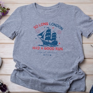 May include: Gray t-shirt with a blue and red graphic of a ship sailing away from fireworks. The text reads "So Long London Had a Good Run Signed America 1776".