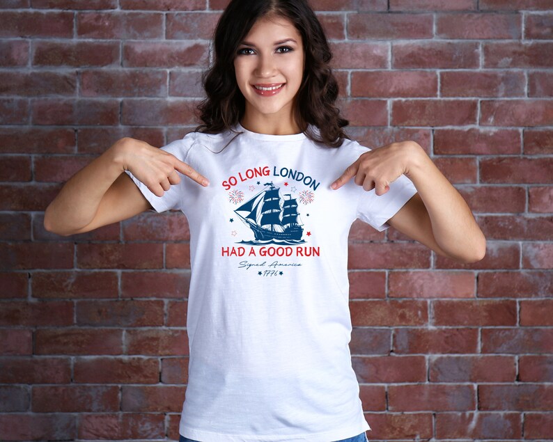May include: White t-shirt with a blue and red graphic of a ship sailing away from a city skyline. The text on the shirt reads "So Long London Had a Good Run Squad America 1776".