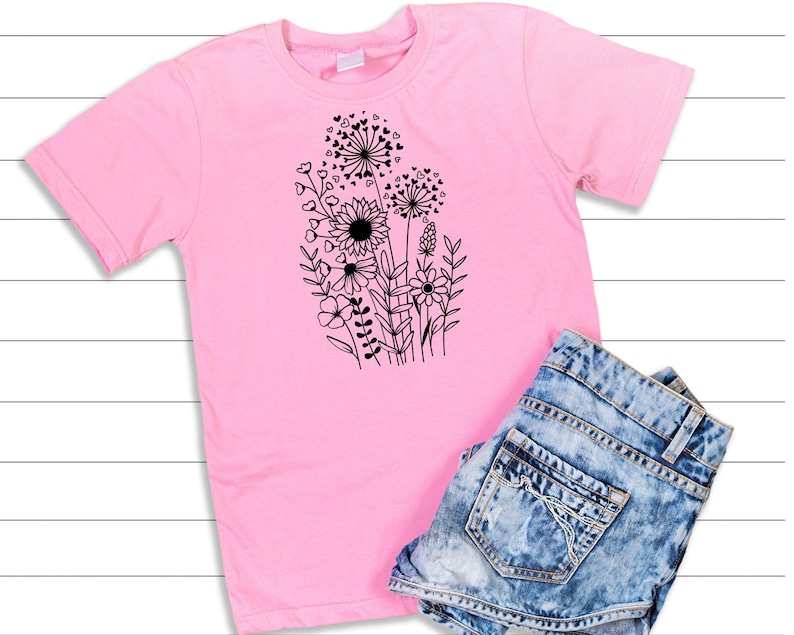 May include: A pink t-shirt with a black graphic of a bouquet of flowers with hearts. The flowers are stylized and include a sunflower, dandelions, and other blooms.