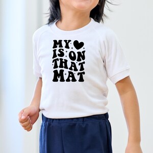 May include: White t-shirt with black text that reads "MY &hearts; IS ON THAT MAT" in a retro font.