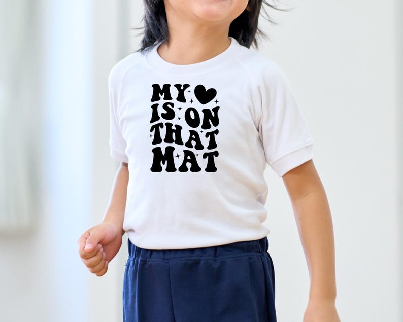 May include: White t-shirt with black text that reads "MY &hearts; IS ON THAT MAT" in a retro font.