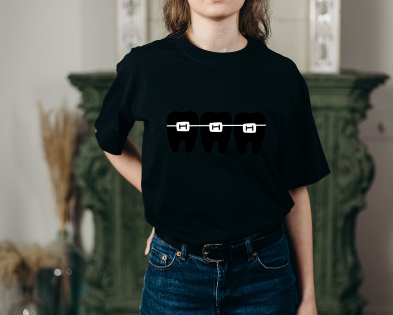 May include: A black t-shirt with a graphic of three teeth with braces. The braces are white and the teeth are black.