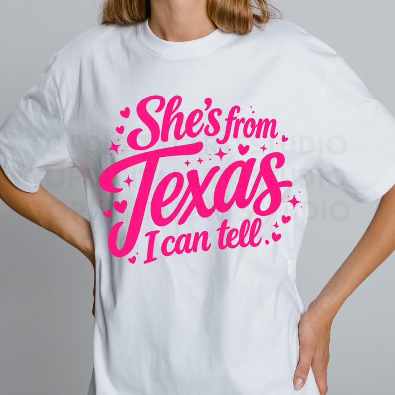 K&ouml;nnte beinhalten: Wei&szlig;es T-Shirt mit dem Text "She's from Texas I can tell" in leuchtendem Pink. Das Design beinhaltet Herzen und Sterne. Das T-Shirt hat einen l&auml;ssigen Stil.