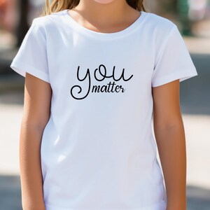 Pode incluir: Camiseta branca com texto preto em letra cursiva que diz "you matter".
