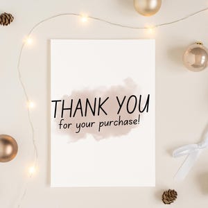 May include: A white card with the text "THANK YOU for your purchase!" written in black. The card is surrounded by gold ornaments and a string of white lights.