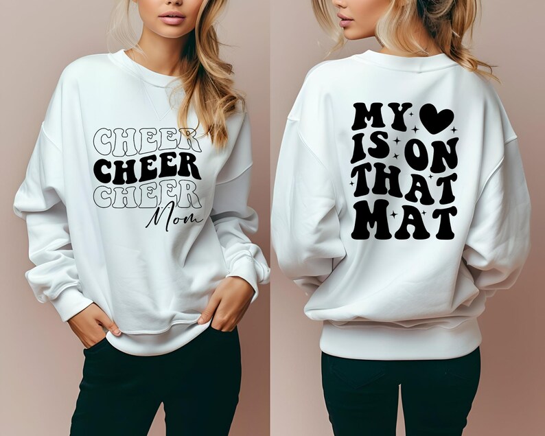 May include: White sweatshirt with black text. The front says "Cheer Cheer Cheer Mom" and the back says "My heart is on that mat".