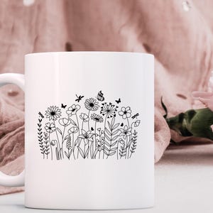 May include: White ceramic mug with a black line drawing of a field of wildflowers and butterflies.