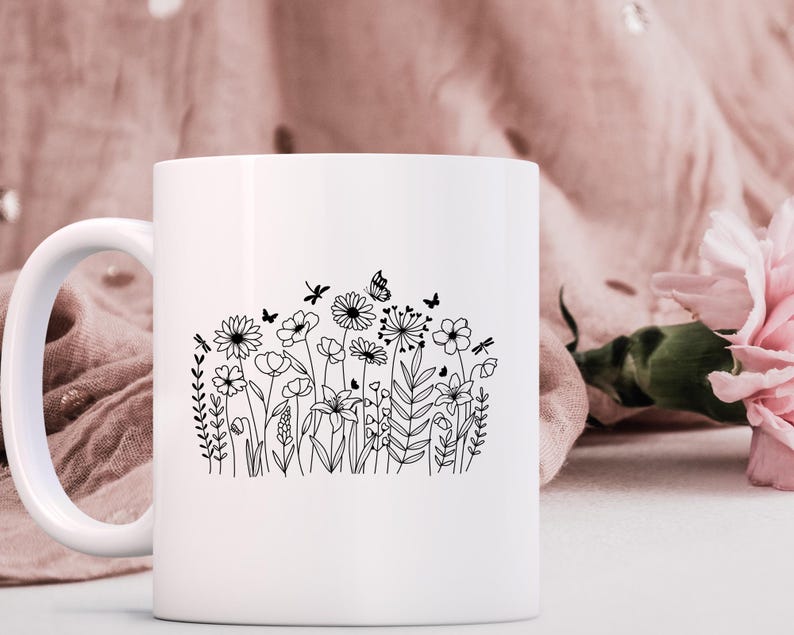 May include: White ceramic mug with a black line drawing of a field of wildflowers and butterflies.