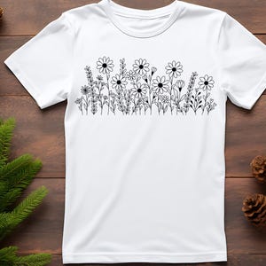 May include: White t-shirt with a black line drawing of a field of flowers.