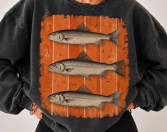 Puede incluir: Una sudadera de cuello redondo gris carbón con un estampado gráfico rectangular de tres peces apilados verticalmente. El fondo del gráfico es de color naranja desgastado con finas rayas verticales blancas y pequeñas siluetas de pájaros negros.