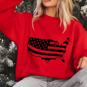 May include: A red sweatshirt featuring a black graphic of the United States map with a flag design. The flag design includes black stripes and stars. The sweatshirt is a solid red color.