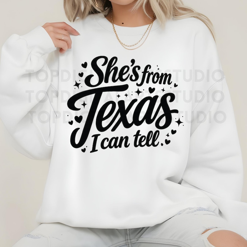 K&ouml;nnte beinhalten: Wei&szlig;es Sweatshirt mit dem Text "She's from Texas I can tell" in schwarzer Schrift. Das Design umfasst kleine Herzen und Sterne. Das Sweatshirt ist ein l&auml;ssiger Stil.