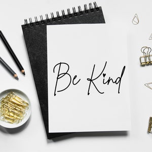 Pode incluir: Uma folha de papel branca com as palavras "Be Kind" escritas em tinta preta em um caderno preto com clipes de pasta dourados e l&aacute;pis sobre uma superf&iacute;cie branca.