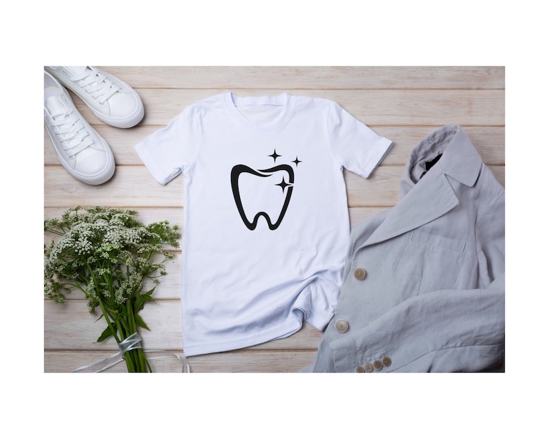 May include: White t-shirt with a black tooth graphic and three stars above it. The shirt is laid flat on a wooden surface with a gray blazer and white sneakers.
