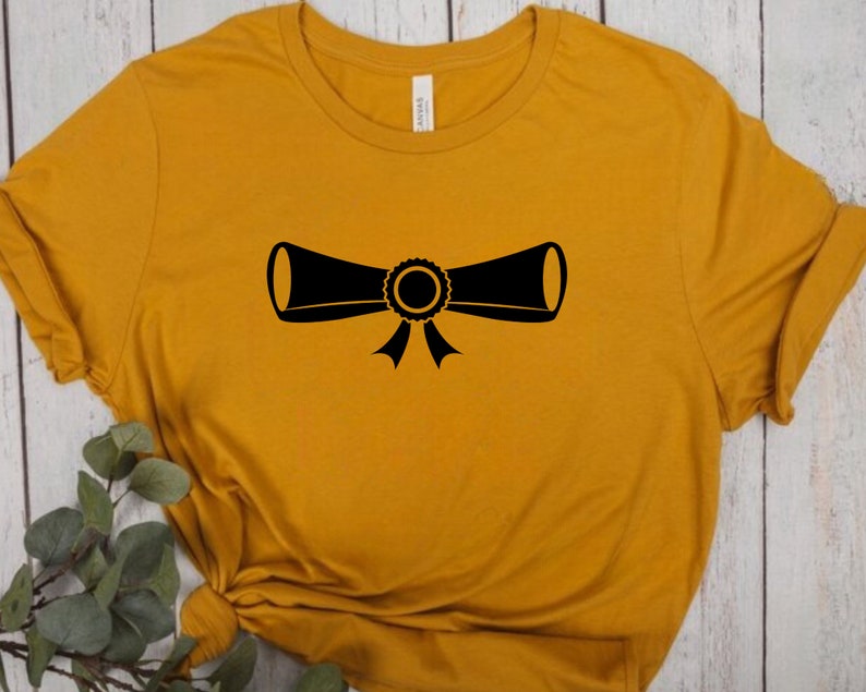 以下が含まれることがあります： マスタードイエローのTシャツに、リボンで結ばれた卒業証書の黒いシルエットが描かれています。