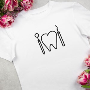 May include: White t-shirt with a black outline of a tooth and dental tools.