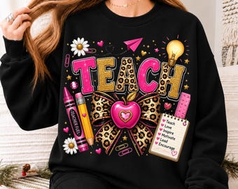 Puede incluir: Una sudadera negra de manga larga con un estampado gráfico de la palabra TEACH en letras rosas y con estampado de leopardo dorado. El diseño incluye una manzana rosa, un lápiz amarillo, un crayón rosa, una bombilla y un bloc de notas con el texto Teach, Love, Inspire, Motivate, Lead, Encourage.