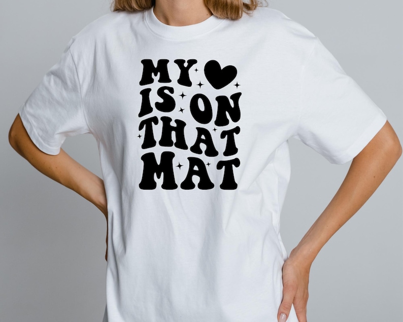 May include: White t-shirt with black text that reads "MY &hearts; IS ON THAT MAT" in a retro font.