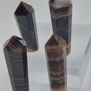 May include: Four brown and beige striped crystal points, also known as wands, are arranged on a white surface. The points are all approximately the same size and shape.