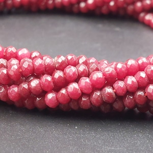 May include: A strand of deep red faceted gemstone beads. The beads are round and have a smooth, polished finish.