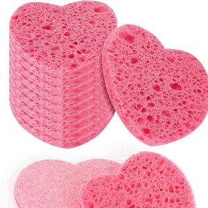 May include: A stack of pink heart-shaped sponges, with two additional sponges on a white background. The sponges are made of a soft, porous material and are ideal for exfoliating and cleansing the skin.