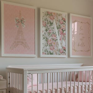 May include: A nursery scene featuring a white crib with pink bedding and a matching dresser. Above the crib are three framed prints: an Eiffel Tower, a floral "A", and a framed quote. The room is decorated in soft pinks and whites, creating a serene atmosphere.