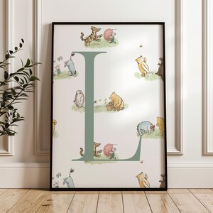 May include: A framed print featuring the letter "L" in a soft green hue, adorned with illustrations of Winnie the Pooh and friends. The artwork includes characters like Tigger, Piglet, and Eeyore, set against a light background.