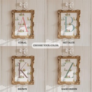 May include: Four framed art prints with gold ornate frames, each featuring a different initial in coral, sky blue, brown, and sage green. The prints have a whimsical animal illustration background. The text "CHOOSE YOUR COLOR:" is in the center.