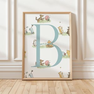 May include: A framed print featuring a large, light blue letter "B" with illustrations of Winnie the Pooh characters. The background is white with small images of the characters. The frame is a light wood color.