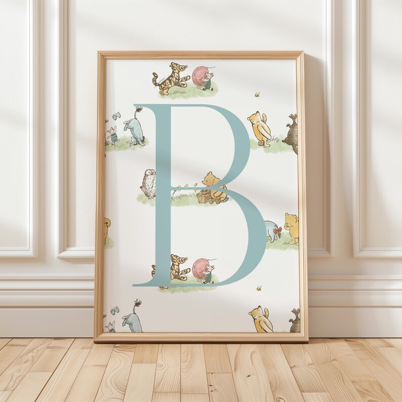 May include: A framed print featuring a large, light blue letter "B" with illustrations of Winnie the Pooh characters. The background is white with small images of the characters. The frame is a light wood color.
