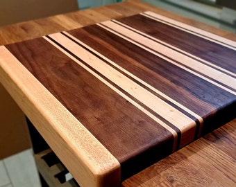 May include: A rectangular wooden cutting board with alternating stripes of light and dark wood. The board has a raised edge around the perimeter.