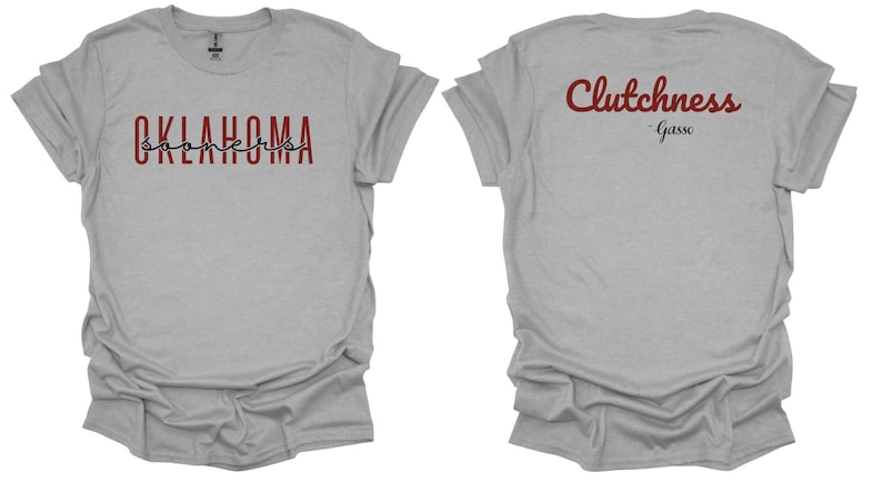 K&ouml;nnte beinhalten: Hellgraues T-Shirt mit den W&ouml;rtern "OKLAHOMA SOONERS" auf der Vorderseite in Burgunderrot und Schwarz. Auf der R&uuml;ckseite des Shirts steht das Wort "Clutchness" in burgunderroter Schrift, darunter "-Gasso". Das Shirt hat kurze &Auml;rmel.