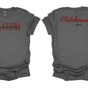 K&ouml;nnte beinhalten: Dunkelgraues T-Shirt mit dem Aufdruck "OKLAHOMA Sooners" in Rot und Schwarz auf der Vorderseite. Auf der R&uuml;ckseite des Shirts steht "Clutchness Garre" in Rot.