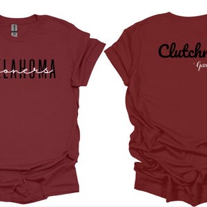 K&ouml;nnte beinhalten: Burgunderfarbene T-Shirts mit Text. Ein Shirt zeigt "OKLAHOMA" in schwarzen Blockbuchstaben mit "sooners" in wei&szlig;er Schrift. Das andere Shirt hat "Clutchness" in schwarzer Schrift und "Gasso" in wei&szlig;er Schrift.