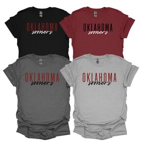 K&ouml;nnte beinhalten: Vier kurz&auml;rmelige T-Shirts in Schwarz, Burgunderrot, Anthrazitgrau und Hellgrau. Jedes Shirt hat das Wort "OKLAHOMA" in fetter, roter Schrift, mit "sooners" in kursiver Schrift darunter. Die Shirts sind aus weichem Material.