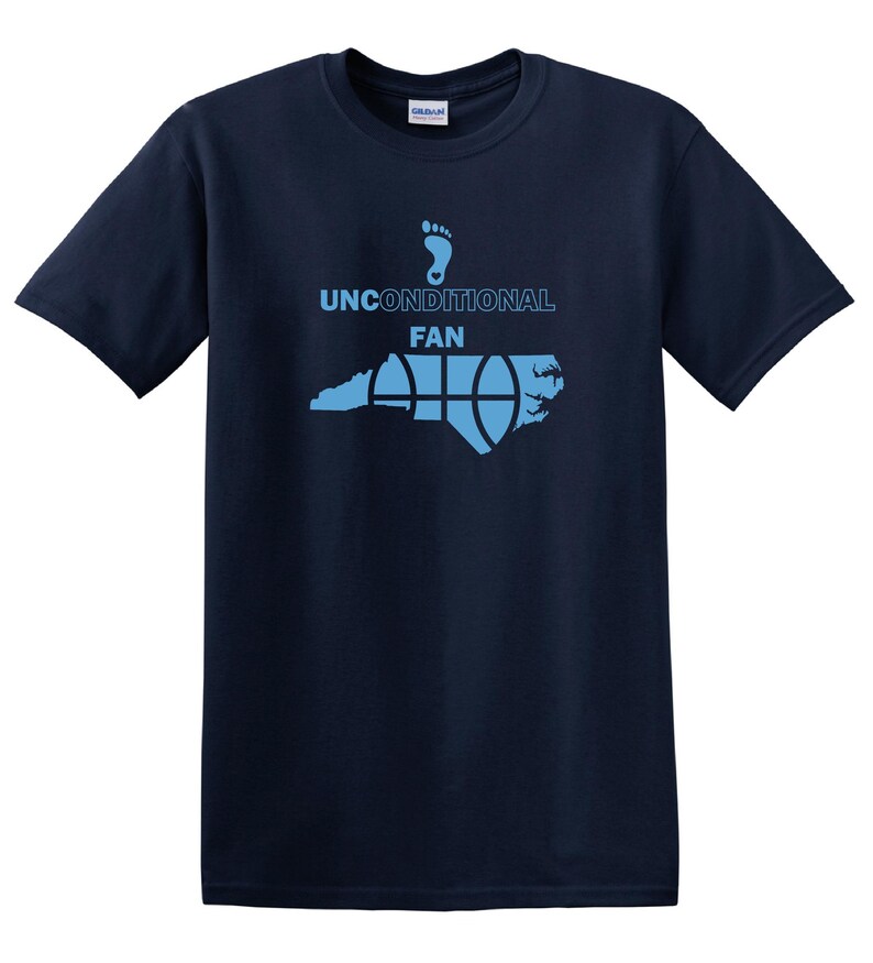K&ouml;nnte beinhalten: Marineblaues T-Shirt mit hellblauer Grafik. Die Grafik zeigt einen Fu&szlig;abdruck, die Worte "UNCONDITIONAL FAN" und ein Basketball-Design &uuml;ber einer Umrisslinie des Bundesstaates North Carolina. Ein Gildan-Etikett ist sichtbar.