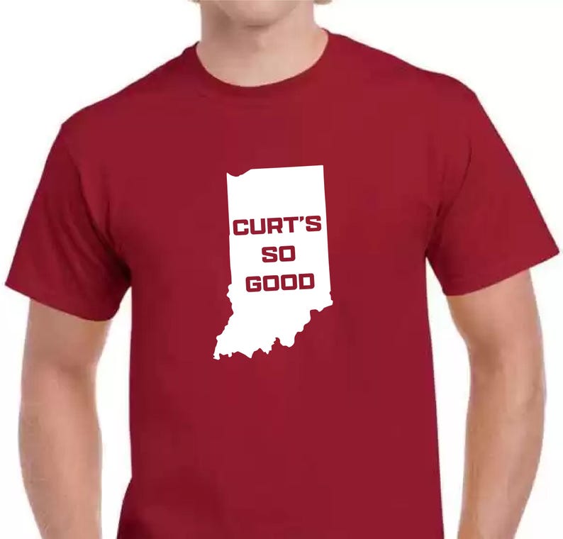 May include: A maroon t-shirt featuring a white outline of the state of Indiana with the words "CURT'S SO GOOD" in a bold, sans-serif font. The shirt is a solid color and has short sleeves.