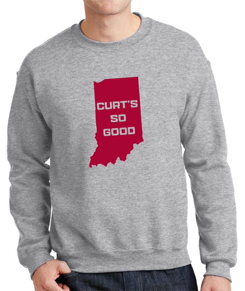 May include: A heather gray sweatshirt with a red graphic of the state of Indiana. The graphic includes the text "CURT'S SO GOOD" in white letters. The sweatshirt is a crew neck style.
