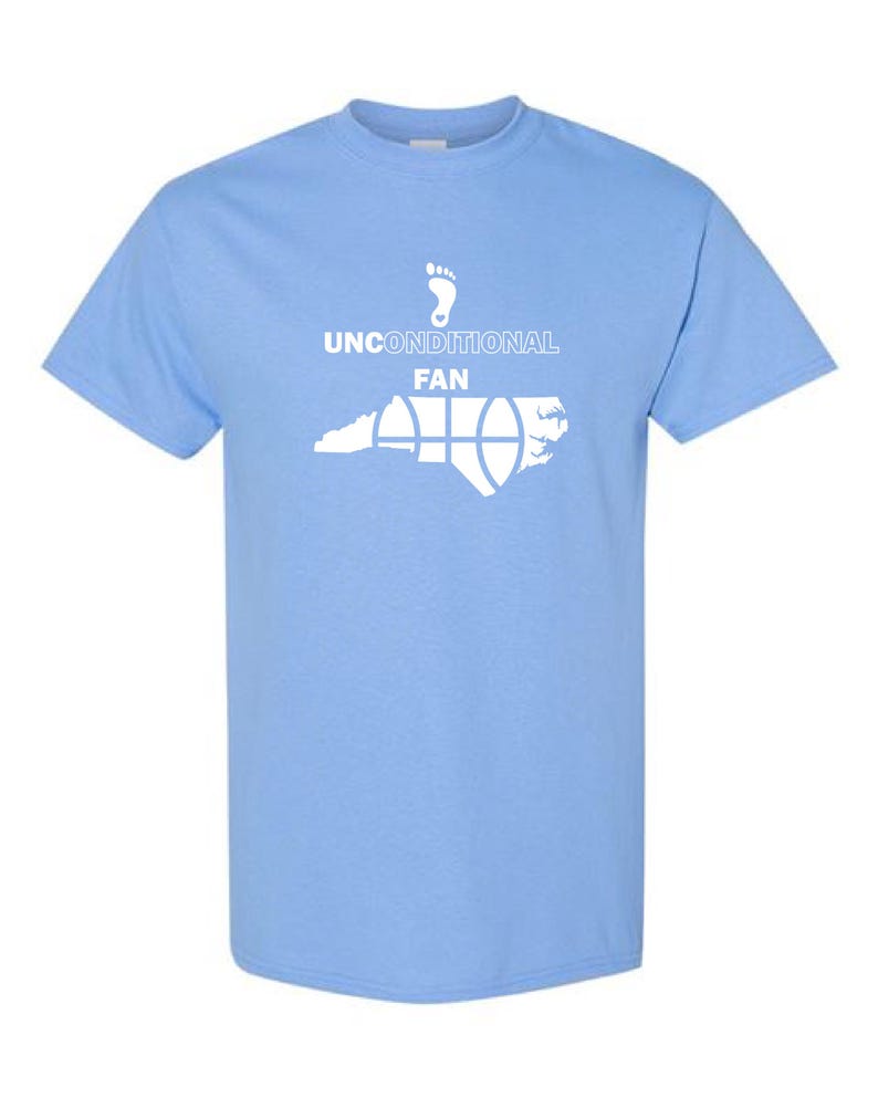 K&ouml;nnte beinhalten: Hellblaues T-Shirt mit wei&szlig;er Grafik. Die Grafik zeigt einen Fu&szlig;abdruck, die Worte "UNCONDITIONAL FAN" und eine stilisierte Abbildung des Bundesstaates North Carolina mit einem Basketball-Design. Das T-Shirt hat kurze &Auml;rmel und einen Rundhalsausschnitt.