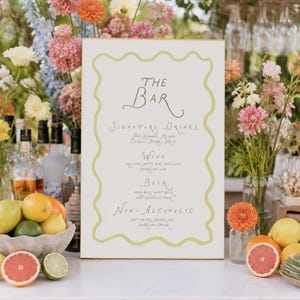 Könnte beinhalten: Ein rechteckiges, weißes Bar-Menüschild mit einem wellenförmigen, hellgrünen Rand. Der Text lautet: The Bar, Signature Drinks, Pink Lemonade Mimosa, Classic Aperol Spritz, Wine, Red Wine, White Wine, Pink Wine, Sparkling Wine, Beer, Dark Beer, Light Beer, Non-Alcoholic.