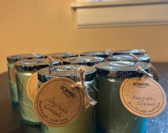 May include: A group of 12 teal blue glass candle jars with black and white patterned lids. Each jar has a brown paper tag with the text "SCENTED CANDLE Berries & Cream Handmade with love".
